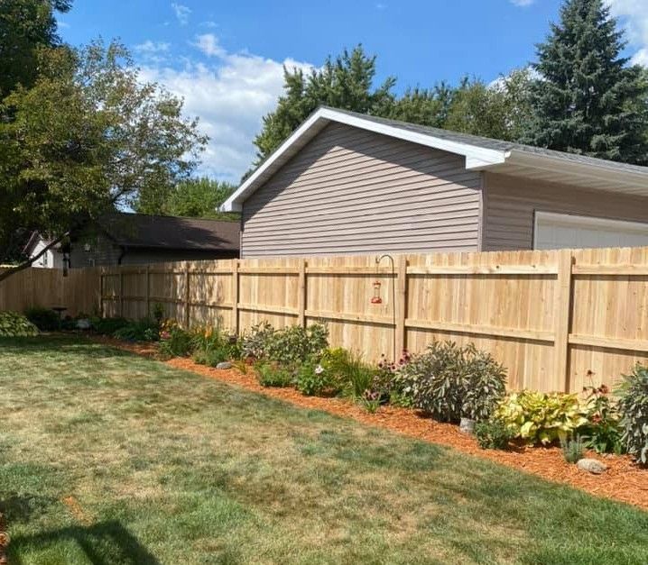 Wooden fence with flower bed along the side of a house, set in a yard.
