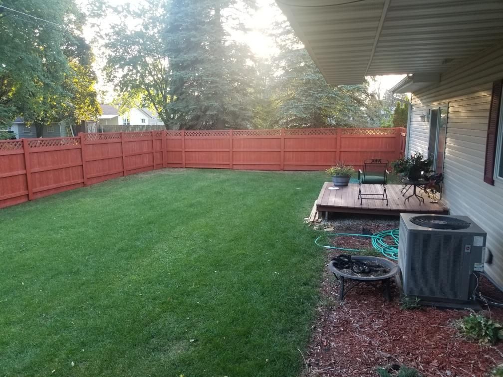 Lush green backyard with a red fence, wooden deck, and air conditioning unit.