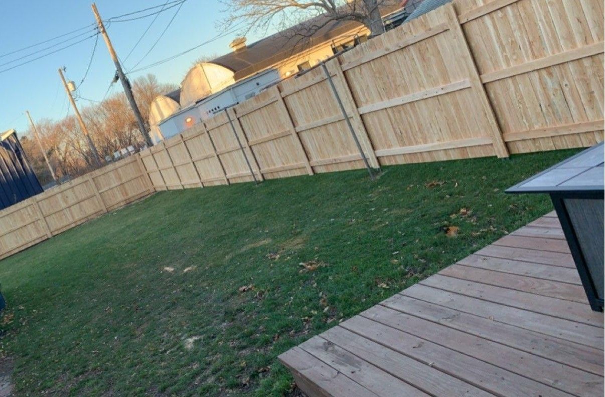 Wooden fence surrounds a grassy backyard, adjacent to a wooden deck.