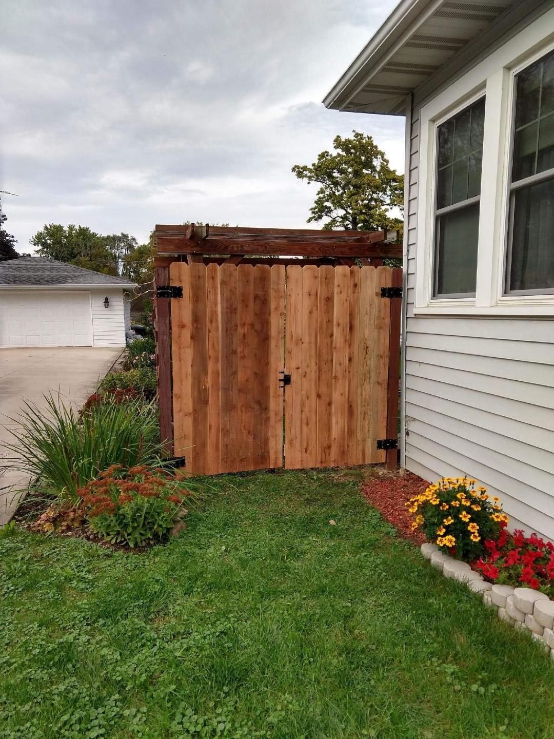 Wooden gate in a yard, beside a house with a white exterior.