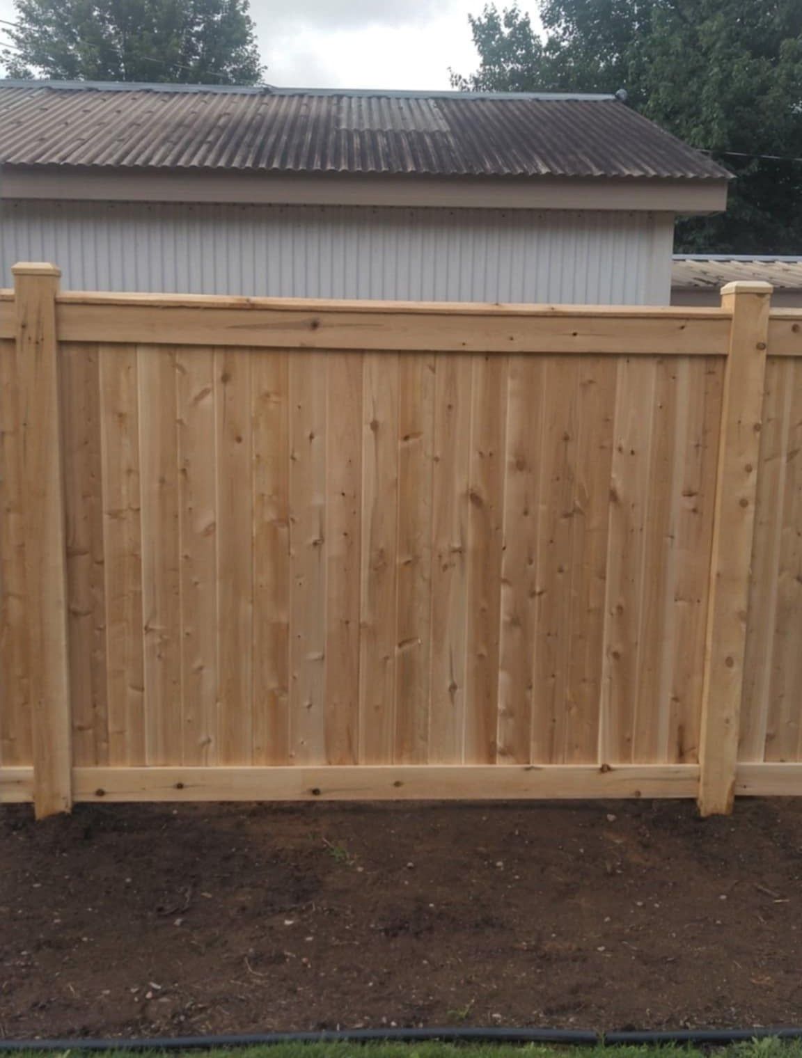 Wooden fence in front of a building with a corrugated roof, set in a dirt bed.