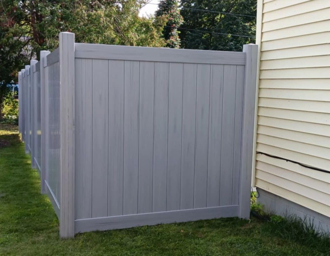 Gray privacy fence beside a yellow house, on a green lawn.