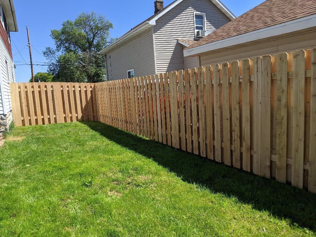 Wooden fence encloses a green lawn in a backyard, sunny day.