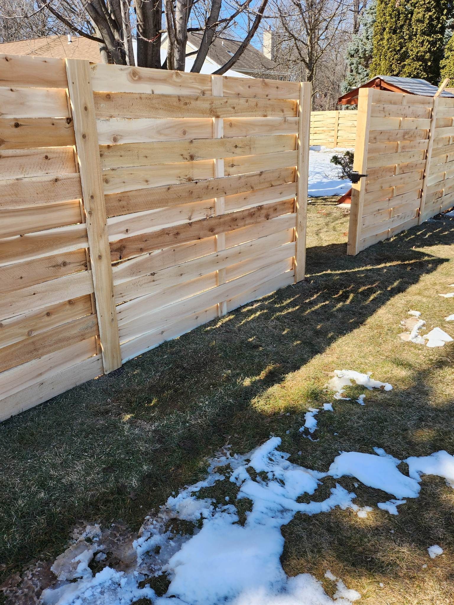New wooden fence being built on a lawn with patches of snow.
