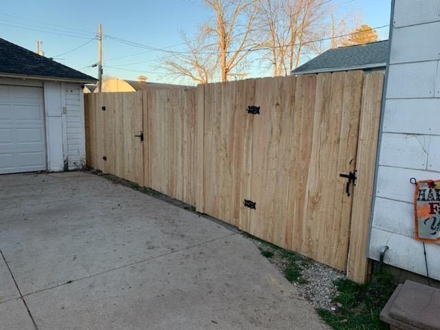 Wooden fence with three gates on a concrete driveway.