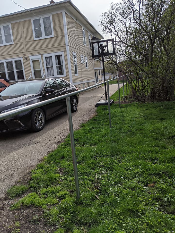 Black car parked near a basketball hoop set up on a grassy area next to a building.