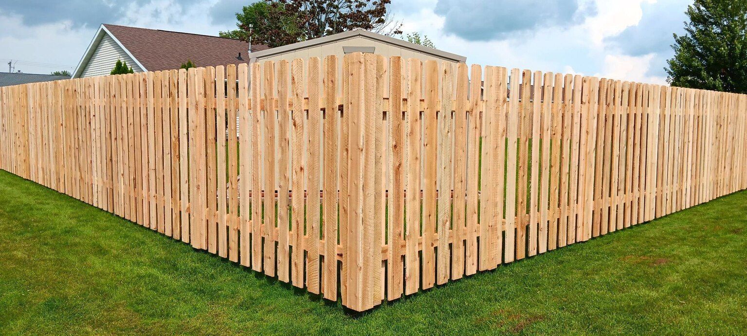 Wooden fence surrounding a grassy yard with houses in the background.