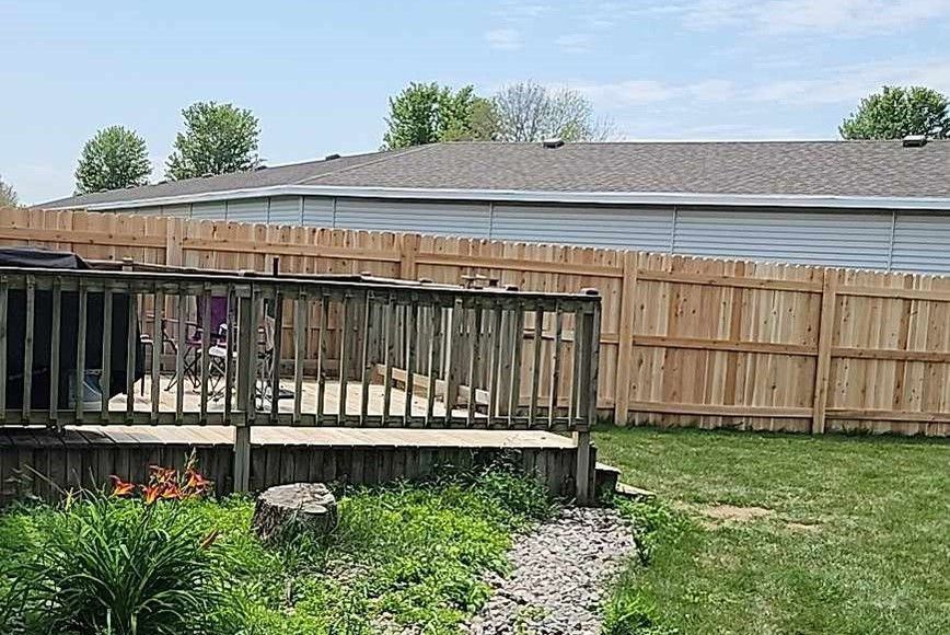 Wooden deck and fence in a backyard, with a lawn and building in the background.