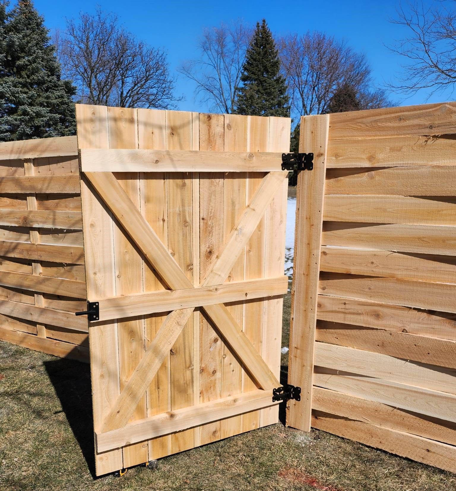 Wooden gate in an open position, part of a wooden horizontal fence, outdoors on a sunny day.