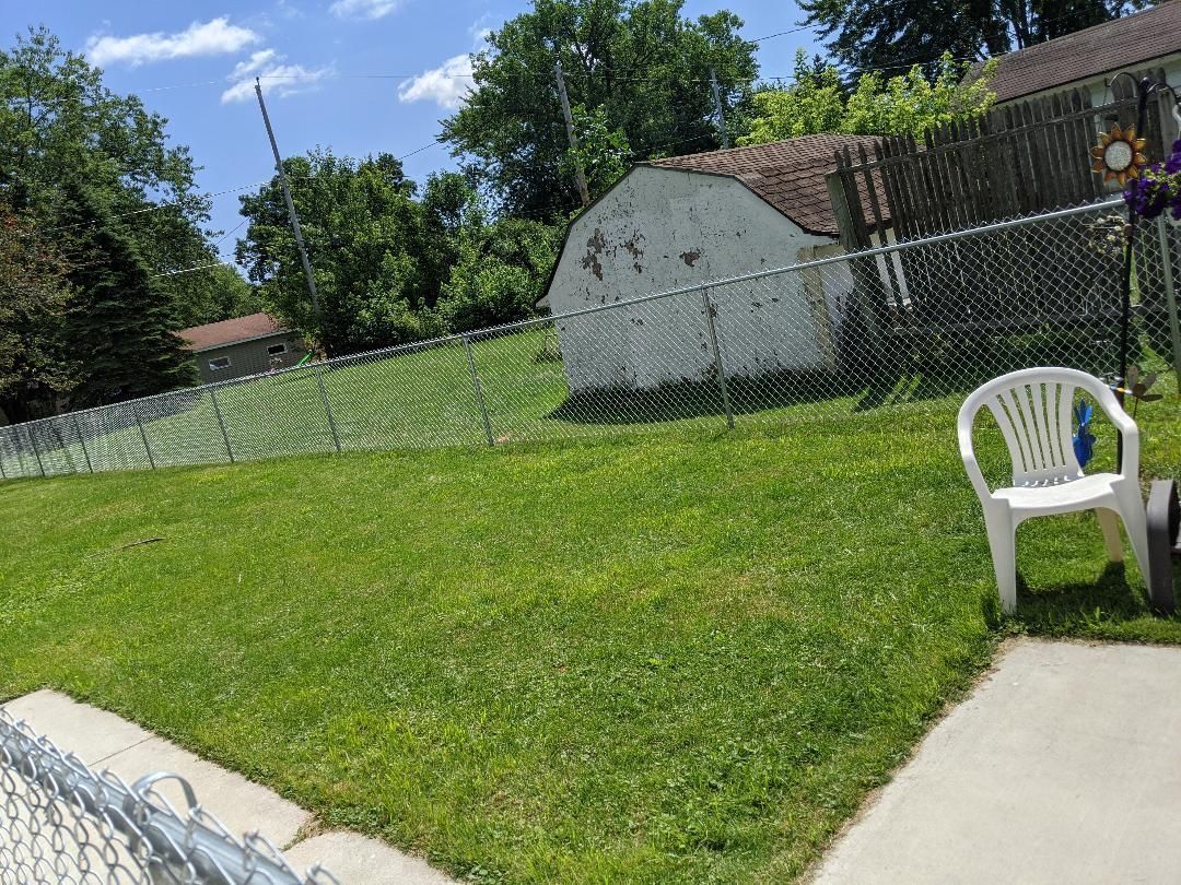 Grassy backyard with chain link fence, white shed, and plastic chair.