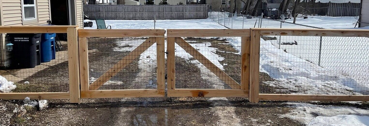Wooden fence and gate with mesh, set in snow-covered yard.