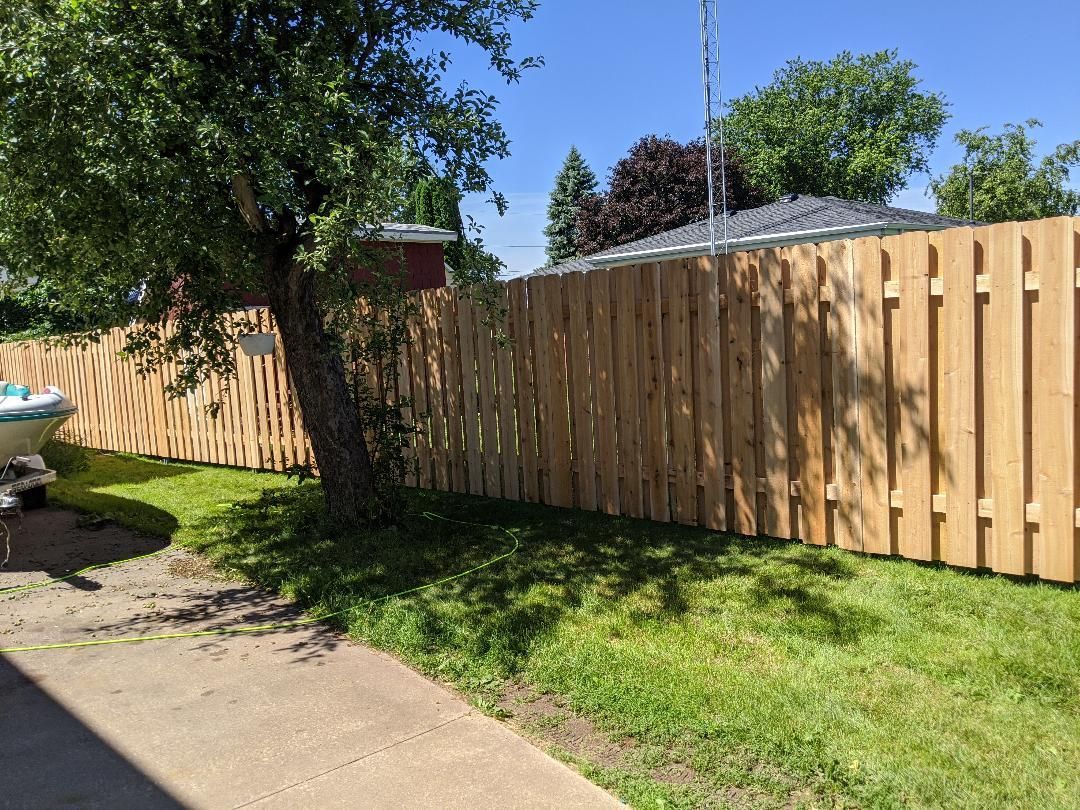Wooden fence in a yard next to a tree, cast shadows on the grass under a bright sky.