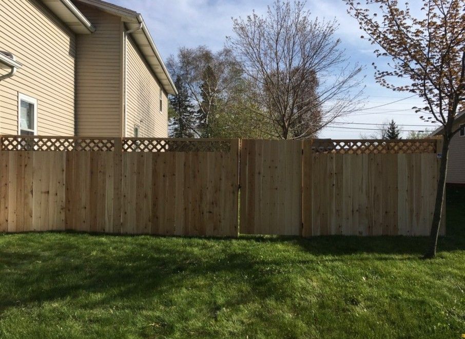 Wooden fence with lattice top in a grassy yard, beside a beige house.