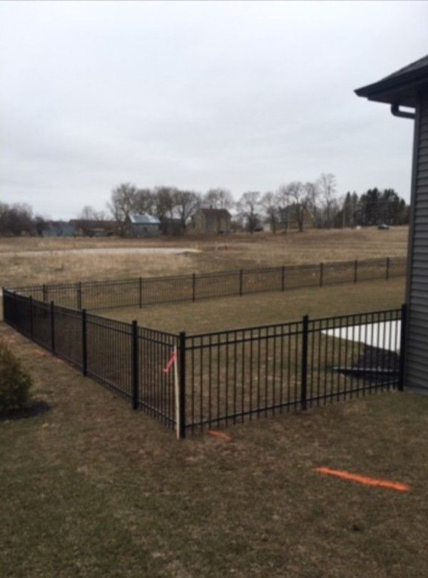 Black metal fence encloses a grassy area in a yard; view of a field, cloudy sky.