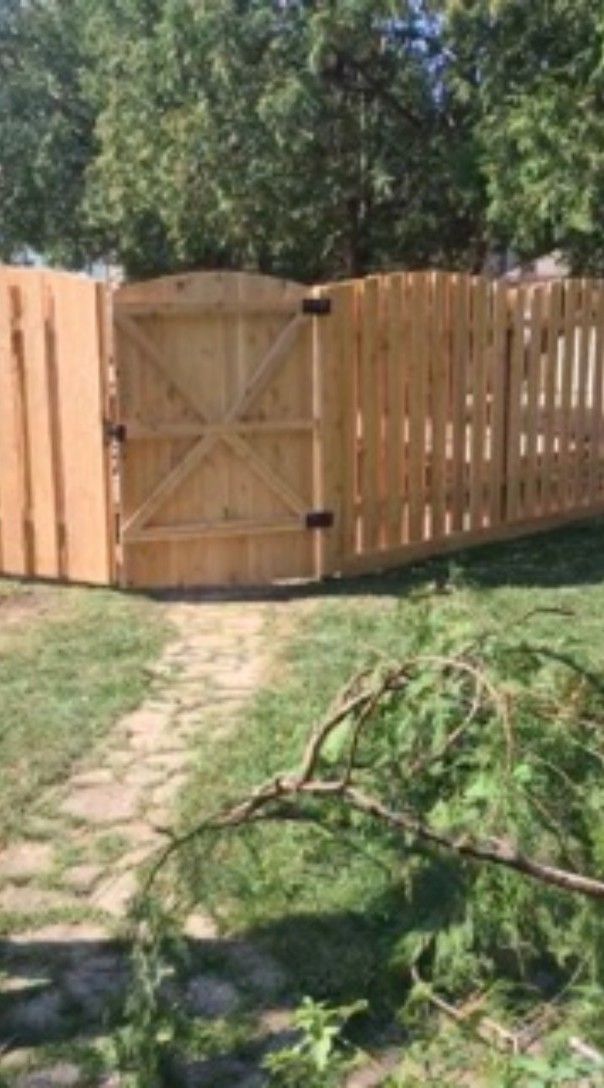 Wooden fence with gate in a yard; path and fallen tree branch in the foreground.