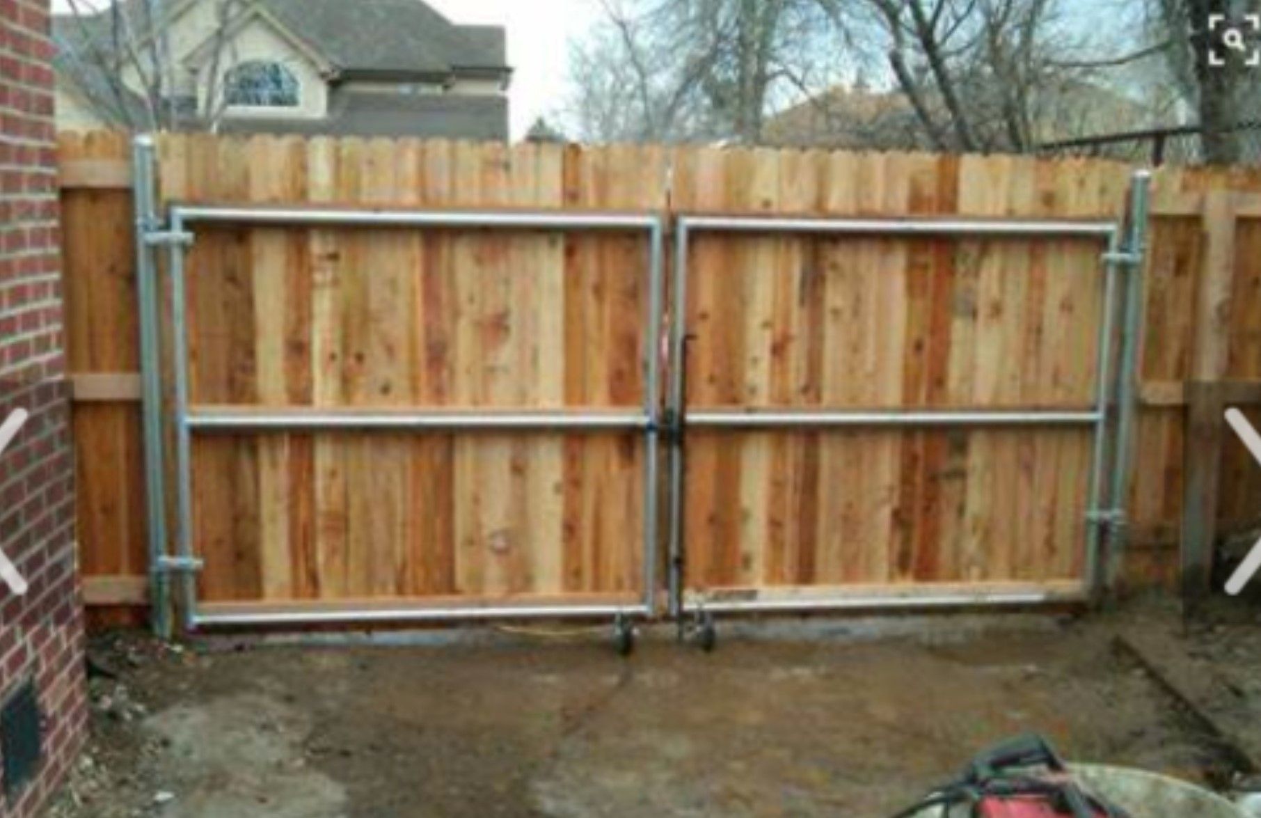 Wooden double gate within a wooden fence, framed by metal, in a yard.