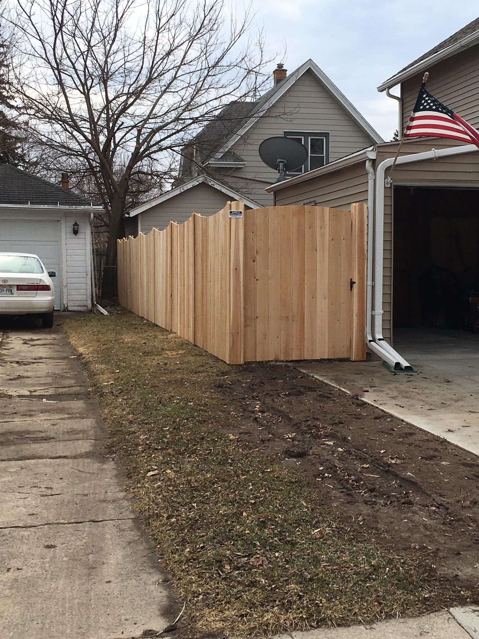 Wooden fence along a driveway with a garage on the left and a garage on the right with an American flag.