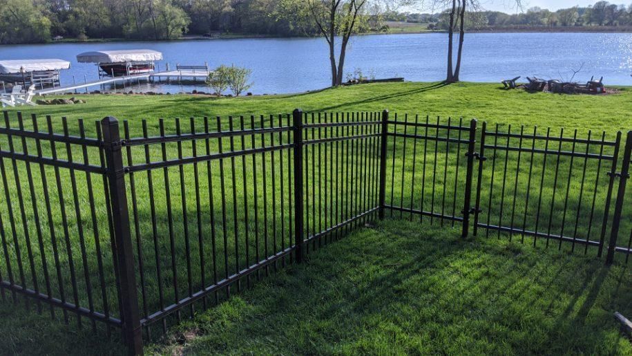 Black metal fence and gates on a grassy lawn with a lake and docks in the background.