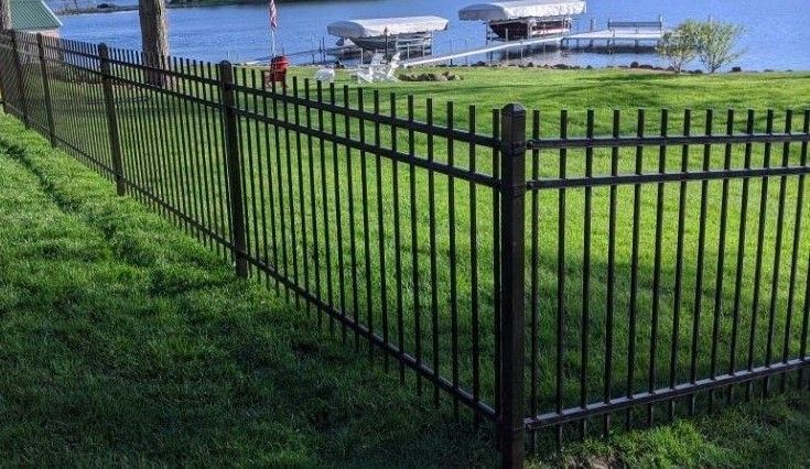 Black metal fence bordering a grassy waterfront yard with boat docks in the background.