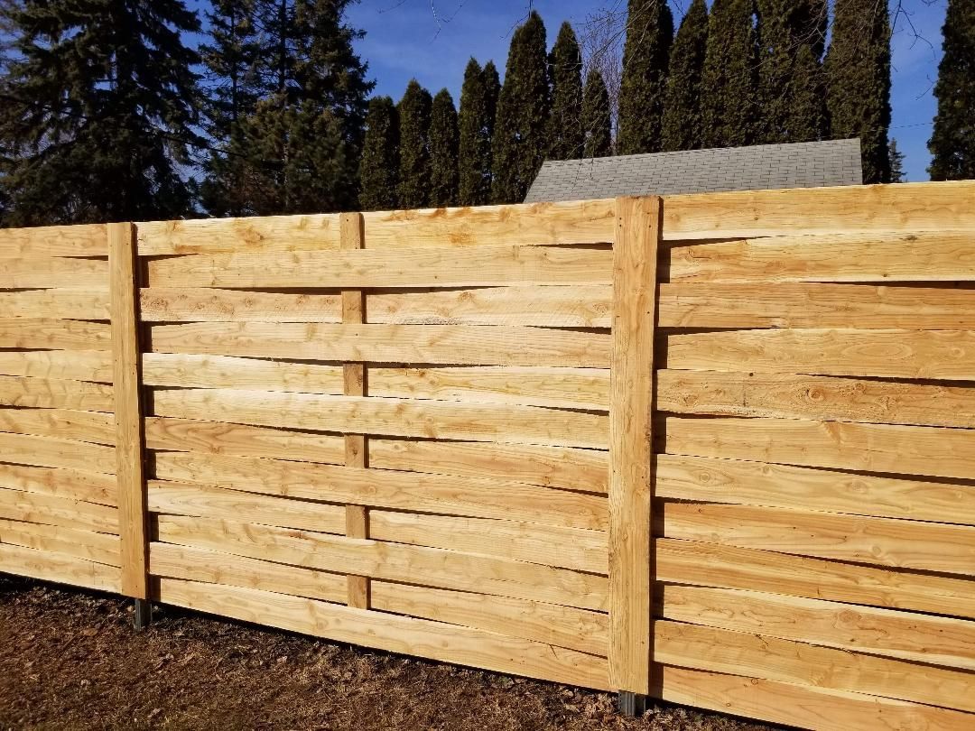 Wooden horizontal slat fence in a yard with trees in the background.