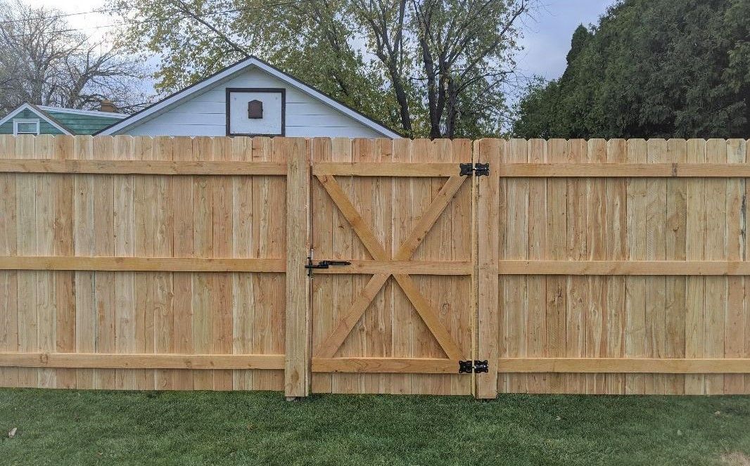 Wooden fence with gate; light brown planks, green grass, house in background.