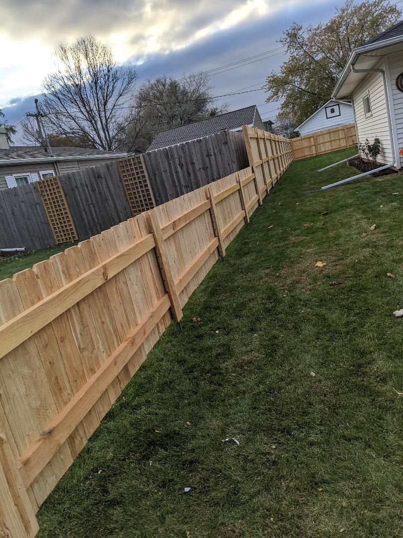 Wooden fence in a backyard with green grass. Cloudy sky in the background.