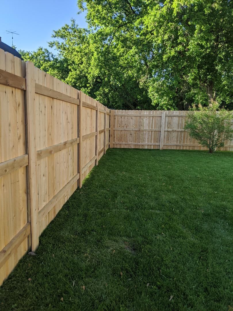 Wooden fence in backyard with green grass and trees.