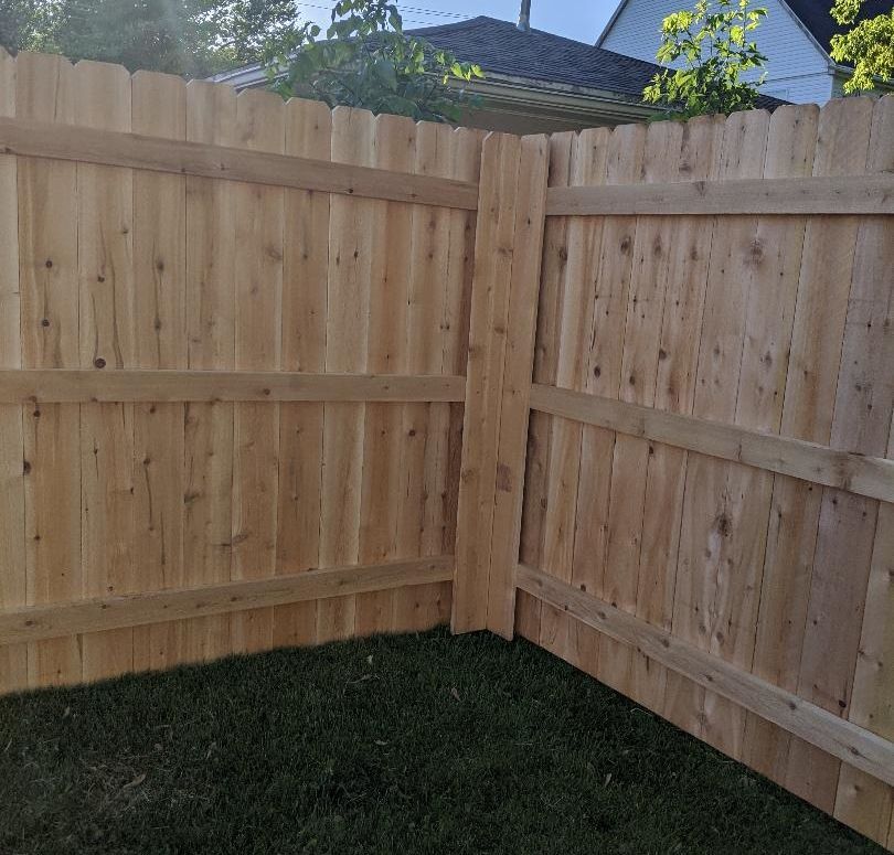Wooden fence corner in a backyard, with green grass.