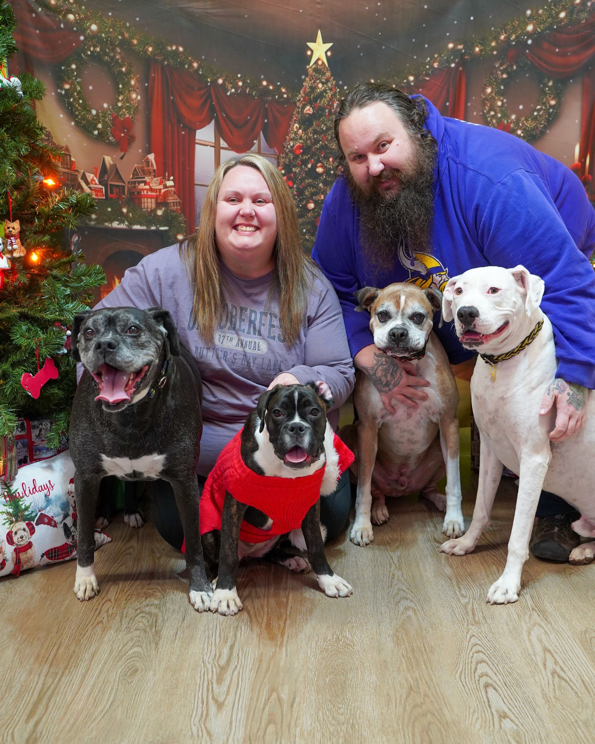 A couple poses with four dogs in front of a Christmas backdrop.