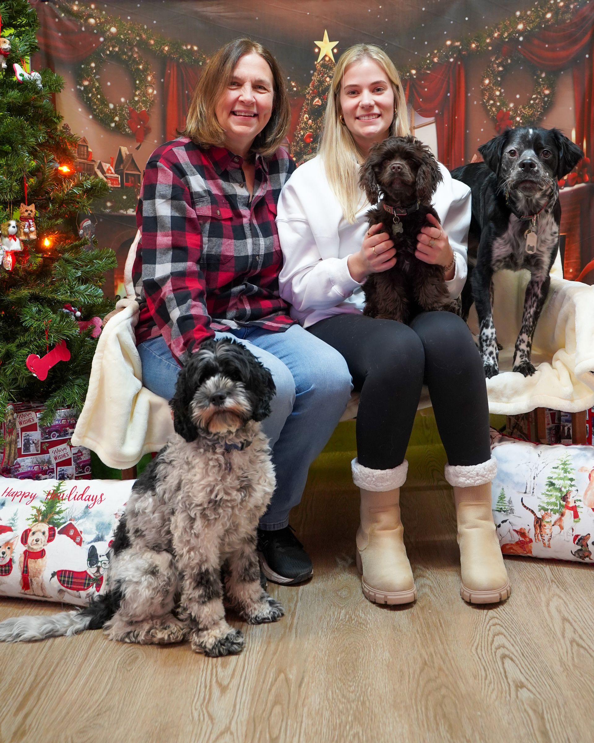 Two women and three dogs pose for a holiday photo near a Christmas tree.