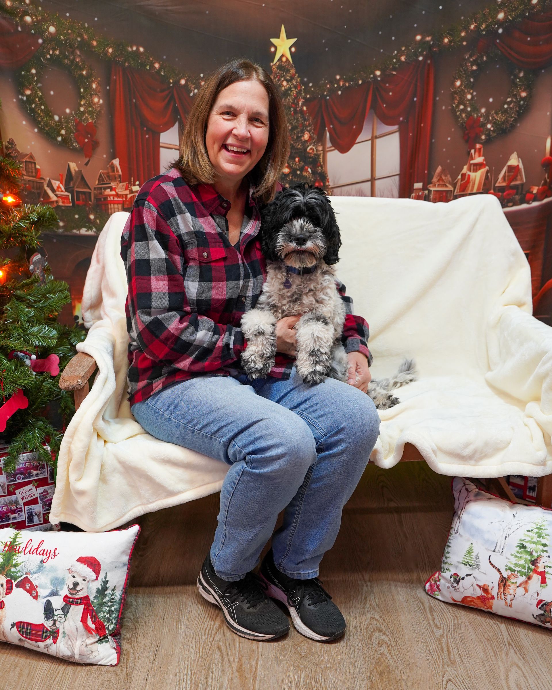 Woman in plaid shirt sits on a bench with a small dog, Christmas backdrop.