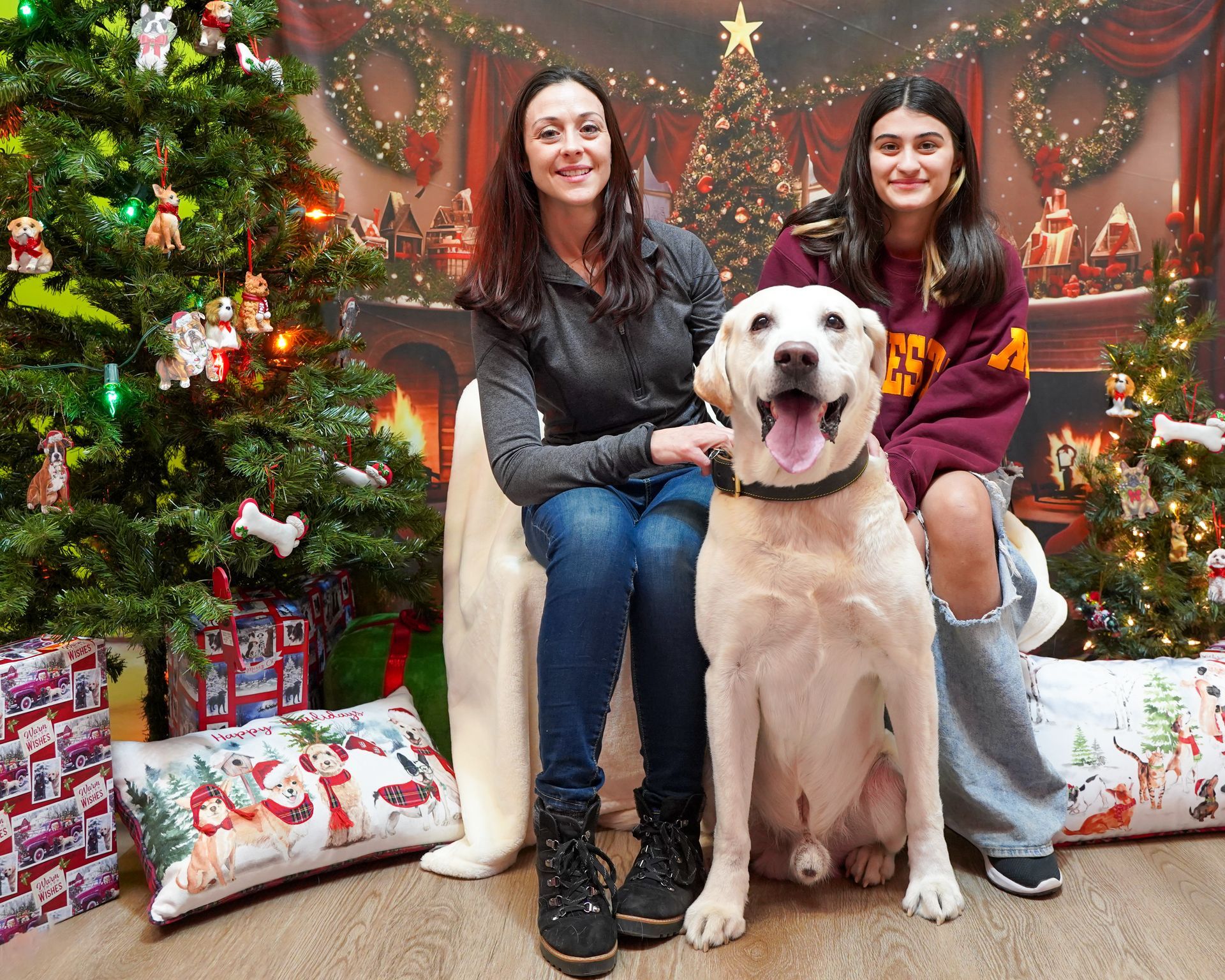 Woman and teen with a yellow lab dog, smiling in front of a Christmas tree backdrop.