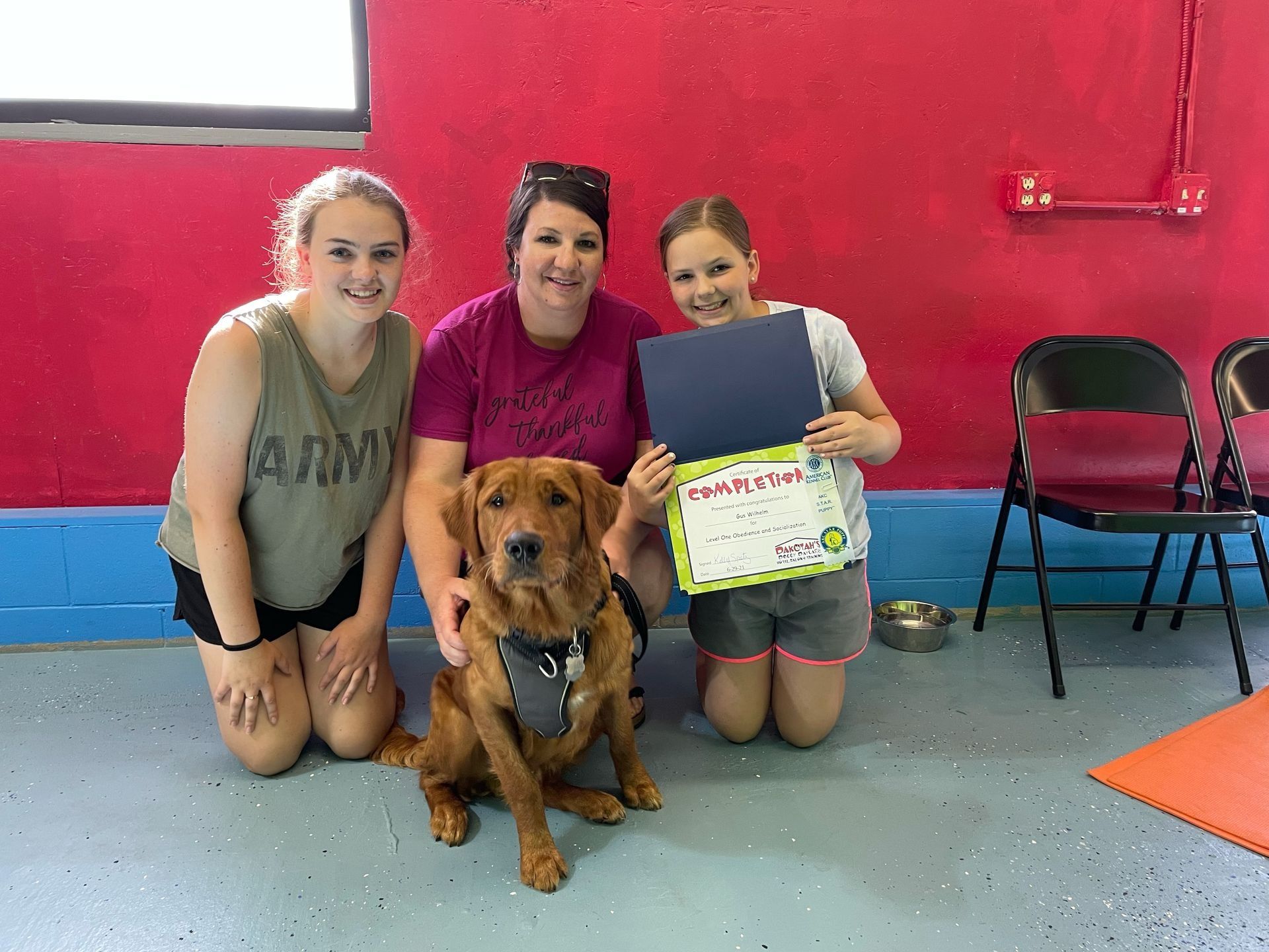 Dog with three people posing, holding a certificate in front of a red and blue wall.
