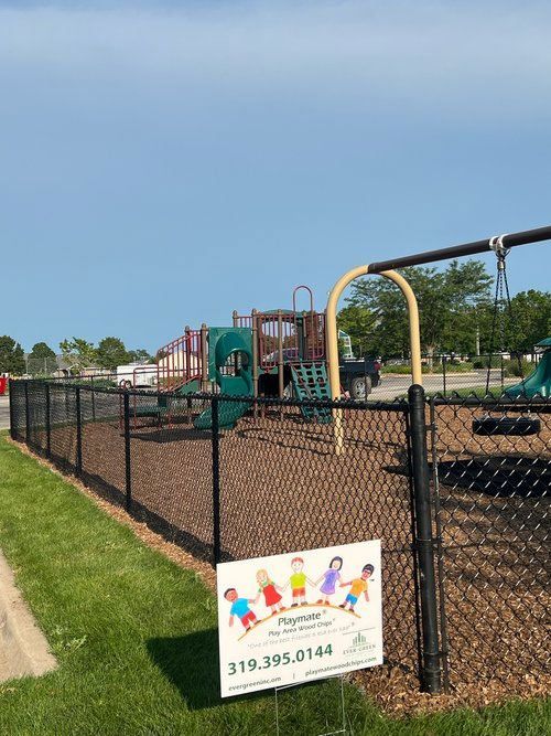 A chain link fence surrounds a playground with a sign in front of it.