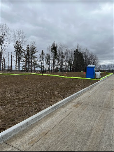 A blue portable toilet is in the middle of a dirt field