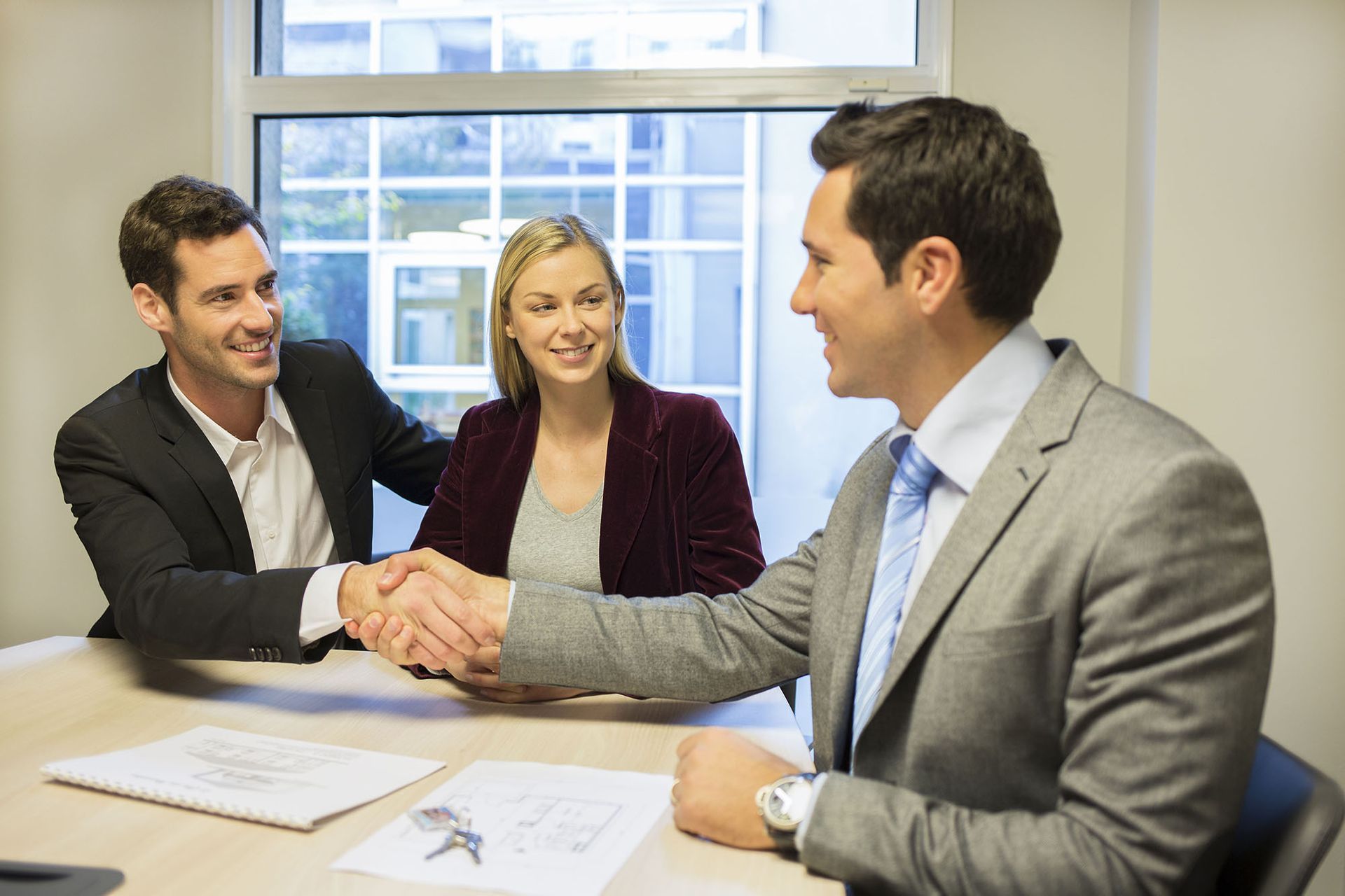 Three businesspeople in a bright office shaking hands during a meeting