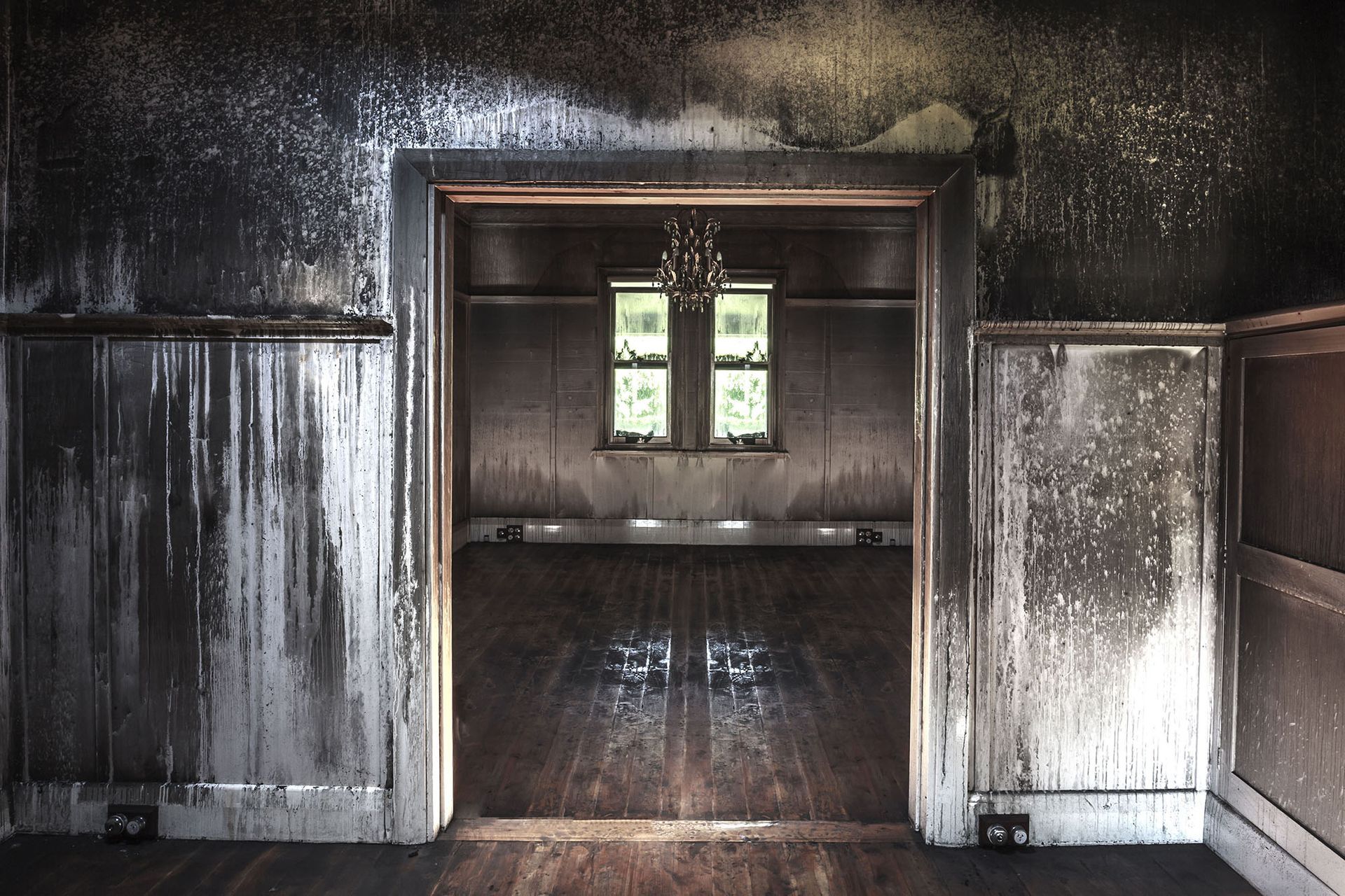 Charred, empty room with a central doorway and two small windows, walls and doorway blackened by smoke