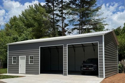 Gray three-bay garage with white trim and a black SUV inside, set among trees under a cloudy sky