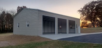 Large gray metal storage building with open garage bays at sunset