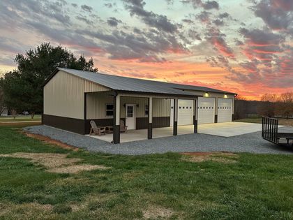 Small tan metal workshop with garage doors at sunset, set on a grassy lot.