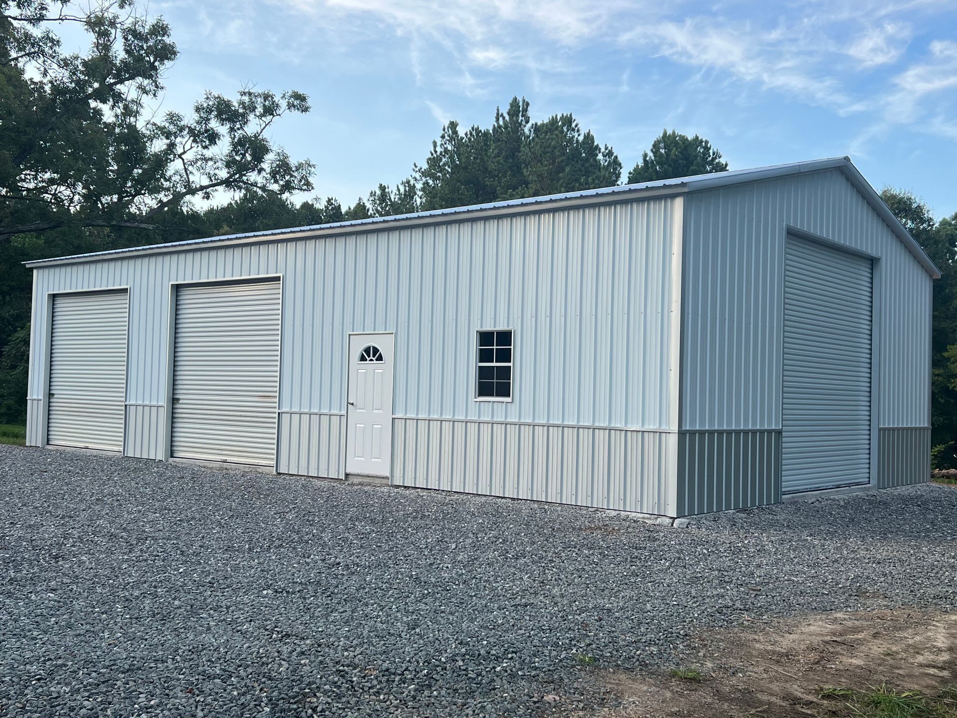 Gray metal storage shed on gravel lot with trees in the background