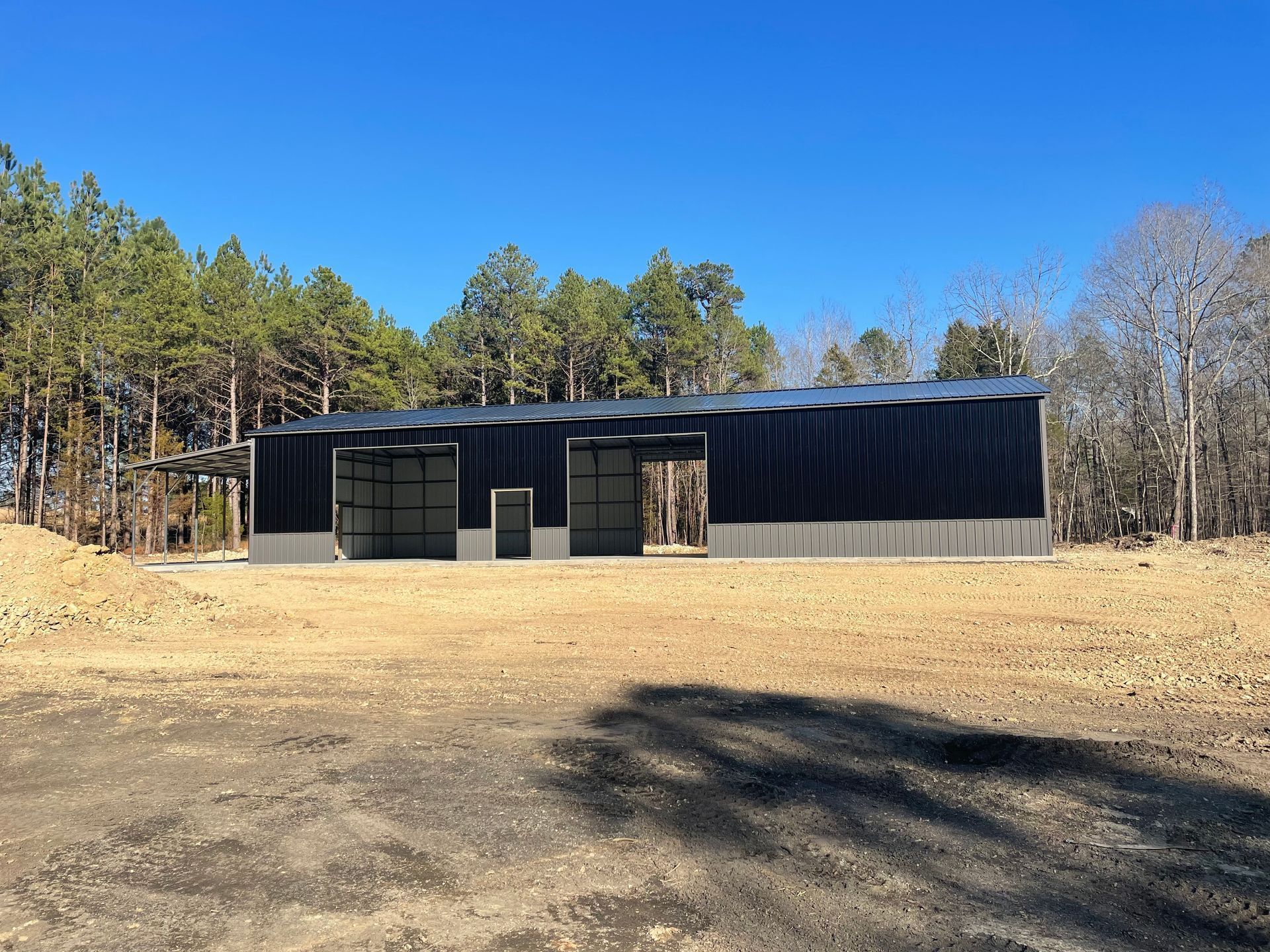 Modern black building on a bare lot, surrounded by trees under a clear blue sky