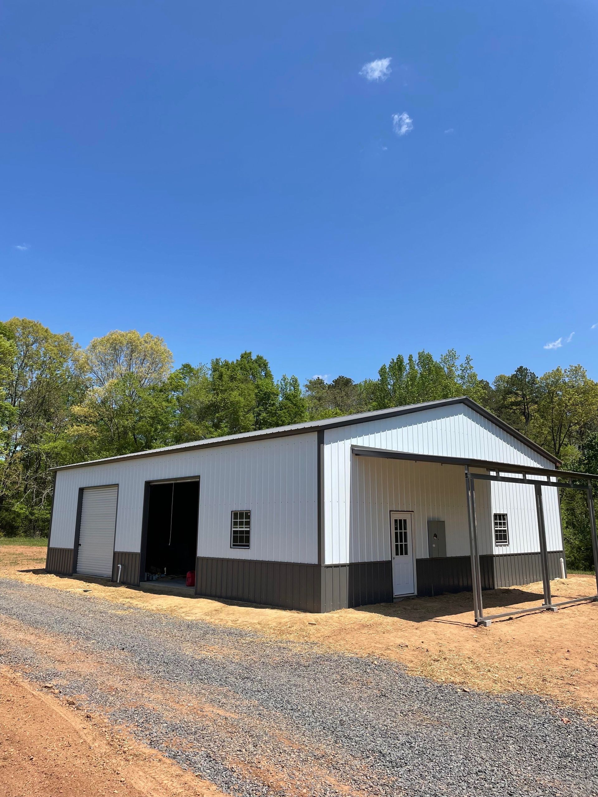 White metal workshop building with open bay door and gravel driveway under a blue sky