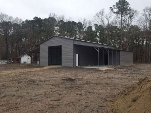 Gray metal barn-like building in a muddy clearing with trees in the background