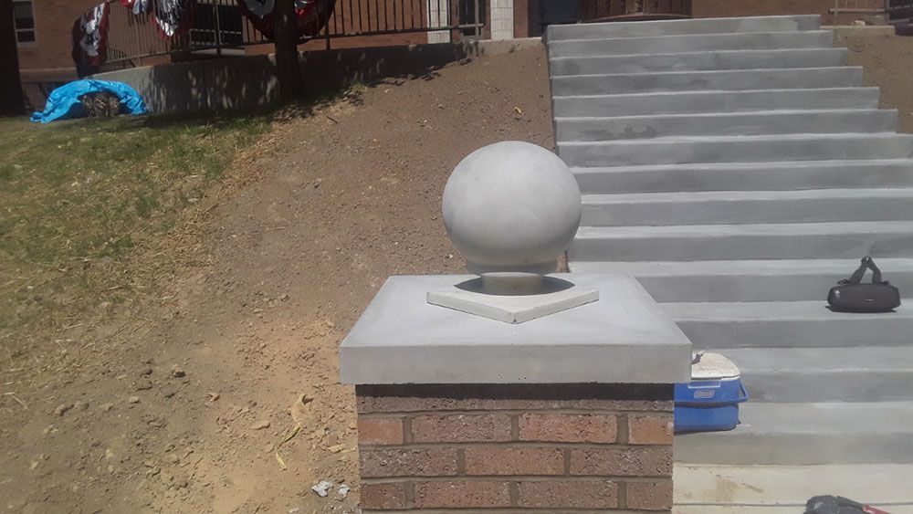 Brick pillar topped with a concrete cap and spherical ornament, stairs in background.