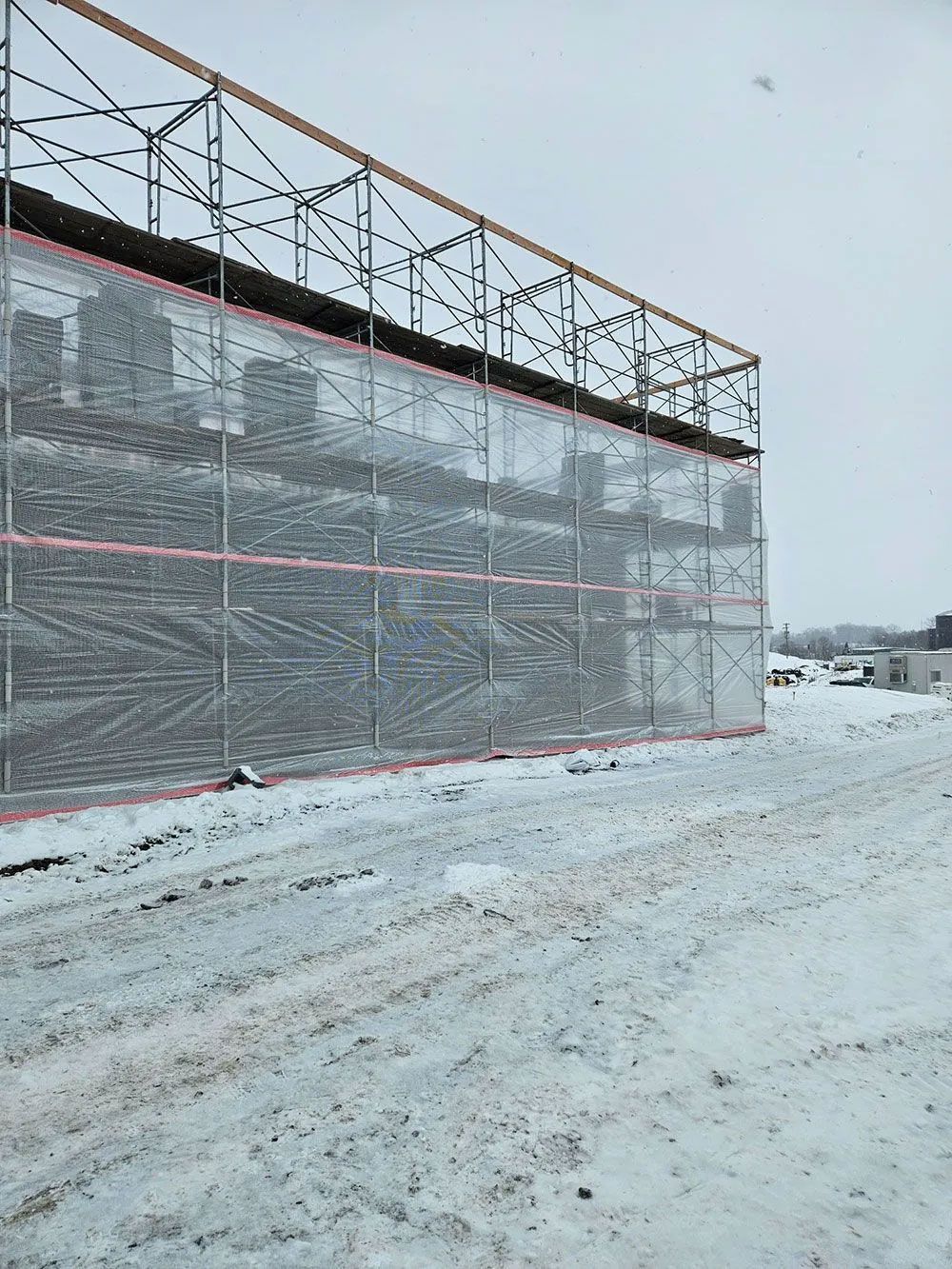 A building under construction is covered in scaffolding and protective sheeting, in a snowy outdoor setting.