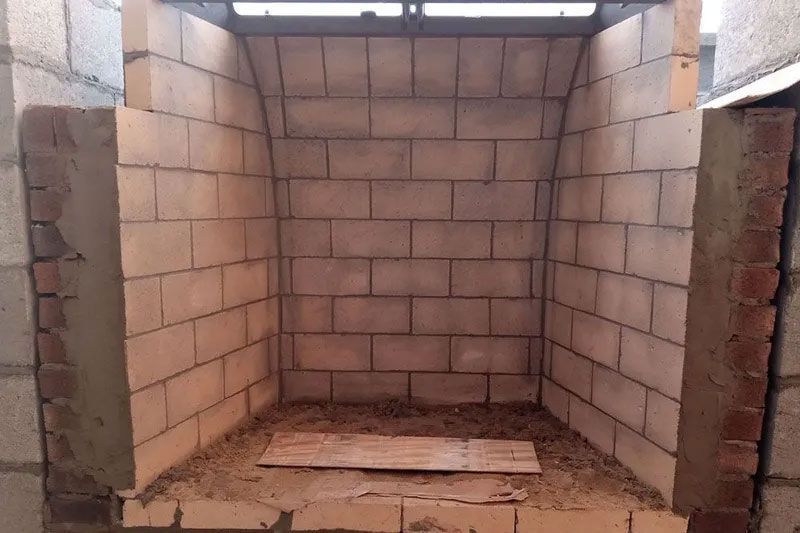 Empty brick fireplace interior, built into a larger brick structure. Tan bricks make up the fireplace, with a curved arch in the back.