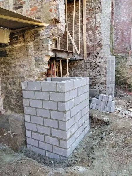 A rectangular concrete block structure under construction, with surrounding brick and debris, in an outdoor setting.