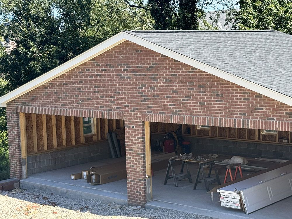 Garage under construction; red brick exterior with exposed wood framing, concrete floor.