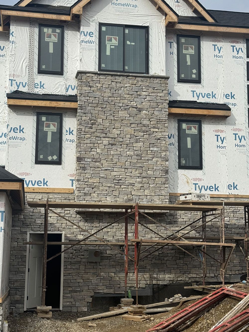 Construction of a multi-story building with a stone chimney and windows. Scaffolding and building materials are visible.